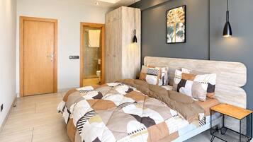Une chambre à coucher moderne, avec un grand lit, une table de chevet, une armoire et une salle de bain visible à travers une porte ouverte.