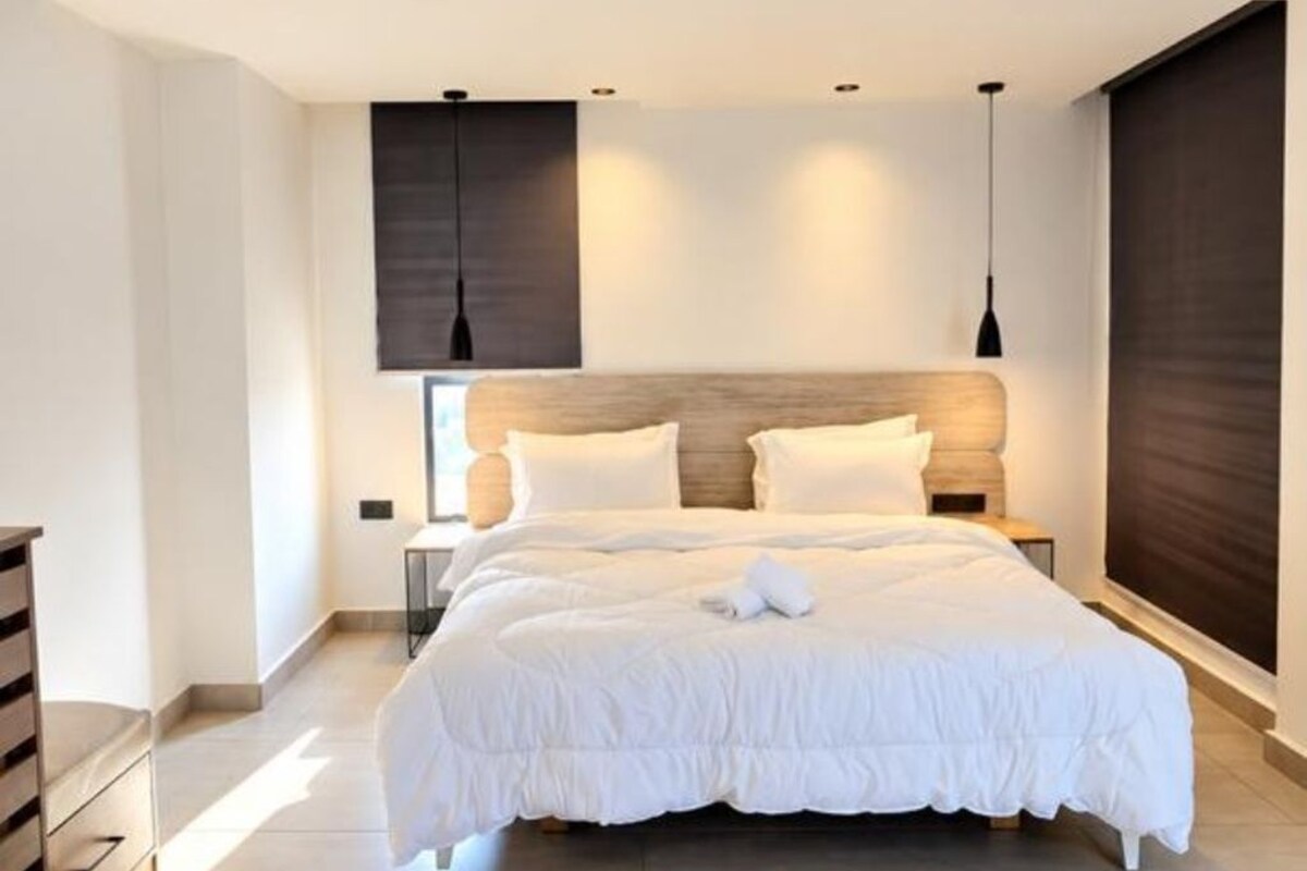 Une chambre moderne avec un grand lit, deux tables de chevet et une tête de lit sombre.