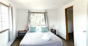 A hotel room with a bed, two bedside tables, a window with curtains, and a door. - Long Stay Cabin 1 - by Hacienda Cuatro Milpas (Ensenada)