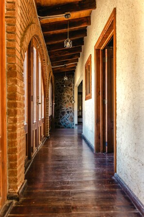 A corridor with wooden flooring, stone walls, and wooden doors. - Long Stay Cabin 1 - by Hacienda Cuatro Milpas (Ensenada)