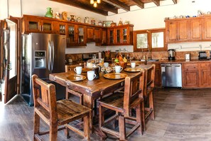 A kitchen with wooden cabinets, a stainless steel refrigerator, and a wooden dining table set with plates and cups. - Long Stay Cabin 1 - by Hacienda Cuatro Milpas (Ensenada)