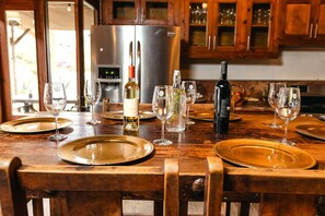 Une table à manger dressée avec des assiettes, des verres et des bouteilles, avec une cuisine en arrière-plan.