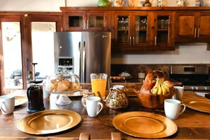 A breakfast setting with a coffee maker, a fruit bowl, and a glass of orange juice on a wooden table. - Long Stay Cabin 1 - by Hacienda Cuatro Milpas (Ensenada)
