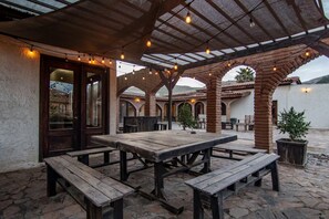 An outdoor patio with a wooden table and benches, surrounded by brick arches and string lights. - Long Stay Cabin 1 - by Hacienda Cuatro Milpas (Ensenada)