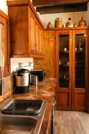 A kitchen with wooden cabinets, a stainless steel sink, and a countertop with a kettle and toaster. - Long Stay Cabin 1 - by Hacienda Cuatro Milpas (Ensenada)