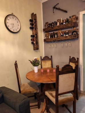 Ein Essbereich mit Holztisch, Stühlen, einer Uhr, Weinflaschen und rustikaler Wandgestaltung.