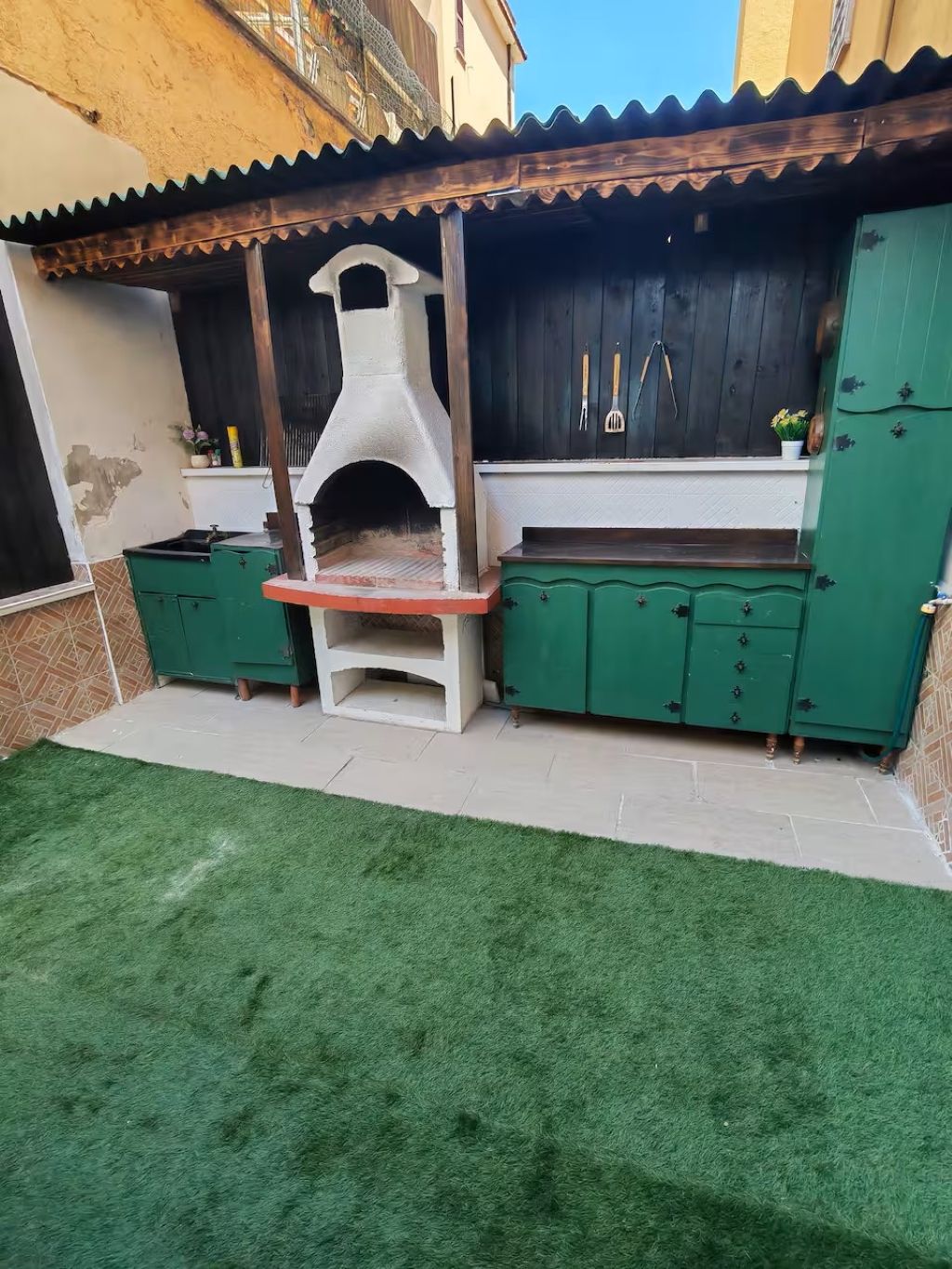 Eine Terrasse mit integriertem Grill und grünen Schränken.