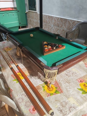 Ein Billardtisch mit grüner Filzoberfläche, umgeben von einer Tischdecke mit Blumenmuster.