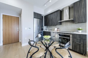 A modern kitchen with a glass dining table, stainless steel appliances, and dark wood cabinetry. - Waterfront Modern 1-Bedroom Condo With Parking (Toronto)