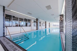 An indoor swimming pool with clear water, steps leading into the pool, and modern interior design. - Waterfront Modern 1-Bedroom Condo With Parking (Toronto)