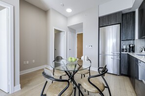 Een moderne keuken met een inbouwkoelkast, een glazen eettafel met stoelen, en een houten deur op de achtergrond.