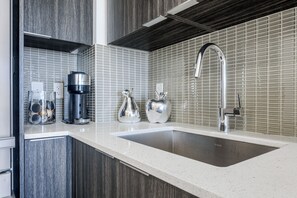 A modern kitchen with a stainless steel sink, a coffee machine, and decorative silver items on the counter. - Waterfront Modern 1-Bedroom Condo With Parking (Toronto)