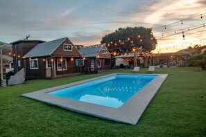 A backyard with a swimming pool, two wooden houses, and string lights. - Long Stay Cabin 2 - by Hacienda Cuatro Milpas (Ensenada)