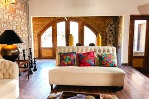 A room with a white sofa, colorful pillows, a lamp, and a brick wall. - Long Stay Cabin 2 - by Hacienda Cuatro Milpas (Ensenada)