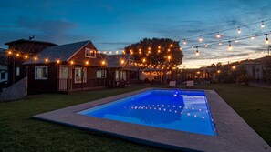 Ein Wohnhaus mit Swimmingpool, Lichterkette und einem Holzhaus.