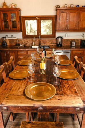 A wooden dining table set with golden plates and wine glasses, surrounded by wooden chairs. - Private Room 2 - Long Stay Hacienda Cuatro Milpas (Ensenada)