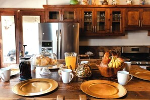 Ein Frühstückstisch mit Kaffeemaschine, Obstschale und Glas Orangensaft.