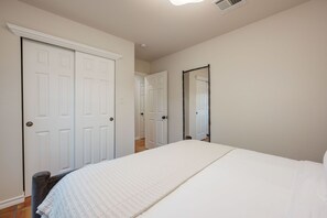 A bedroom with a large bed, two doors, a mirror, and a ceiling vent. - Casa Altura - Hot Tub Desert Retreat - Pet Friendly (Las Cruces)