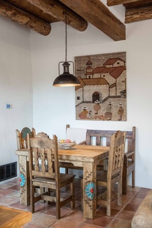 A rustic dining area with a wooden table and chairs, a hanging light fixture, and a wall-mounted painting. - Casa Altura - Hot Tub Desert Retreat - Pet Friendly (Las Cruces)