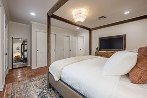 Ein Schlafzimmer mit einem großen Bett, einem Fernseher auf einem Holzständer und einem Spiegel, der den Raum reflektiert.