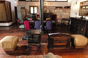 A rustic interior with a vintage stove, leather ottomans, and a stone fireplace. - Private Room - Long Stay Hacienda Cuatro Milpas (Ensenada)