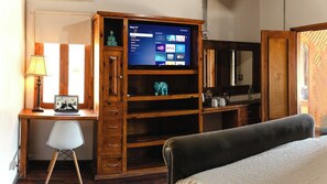 Quarto com estante de madeira para TV, escrivaninha, cadeira e cama.