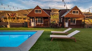 A pool with two lounge chairs, a wooden deck, and two cabins with a view of the hills. - Private Room - Long Stay Hacienda Cuatro Milpas (Ensenada)