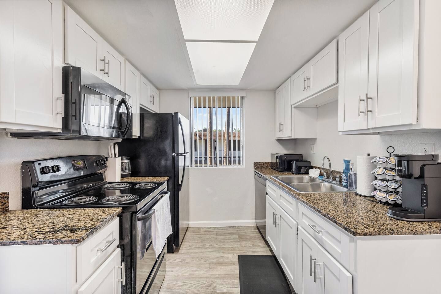 A modern kitchen with white cabinets, a black refrigerator, a stove, and a coffee maker.