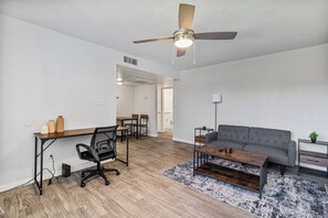 Sala moderna com um sofá cinzento, mesa de centro de madeira e uma escrivaninha com cadeira.