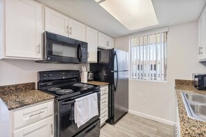 A modern kitchen with white cabinets, a black stove, a stainless steel refrigerator, and a window with vertical blinds. - Convenient Mesa Stay • Close to Everything (Mesa)