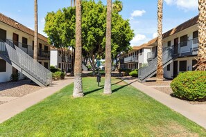 A courtyard with palm trees, a central walkway, and a building with a staircase on the left. - Convenient Mesa Stay • Close to Everything (Mesa)