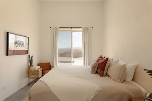 A bedroom with a large bed, a view of the outdoors, a cactus plant, and a framed picture on the wall. - Modern 2-bedroom house with Pool & Spa Joshua Tree (Joshua Tree)
