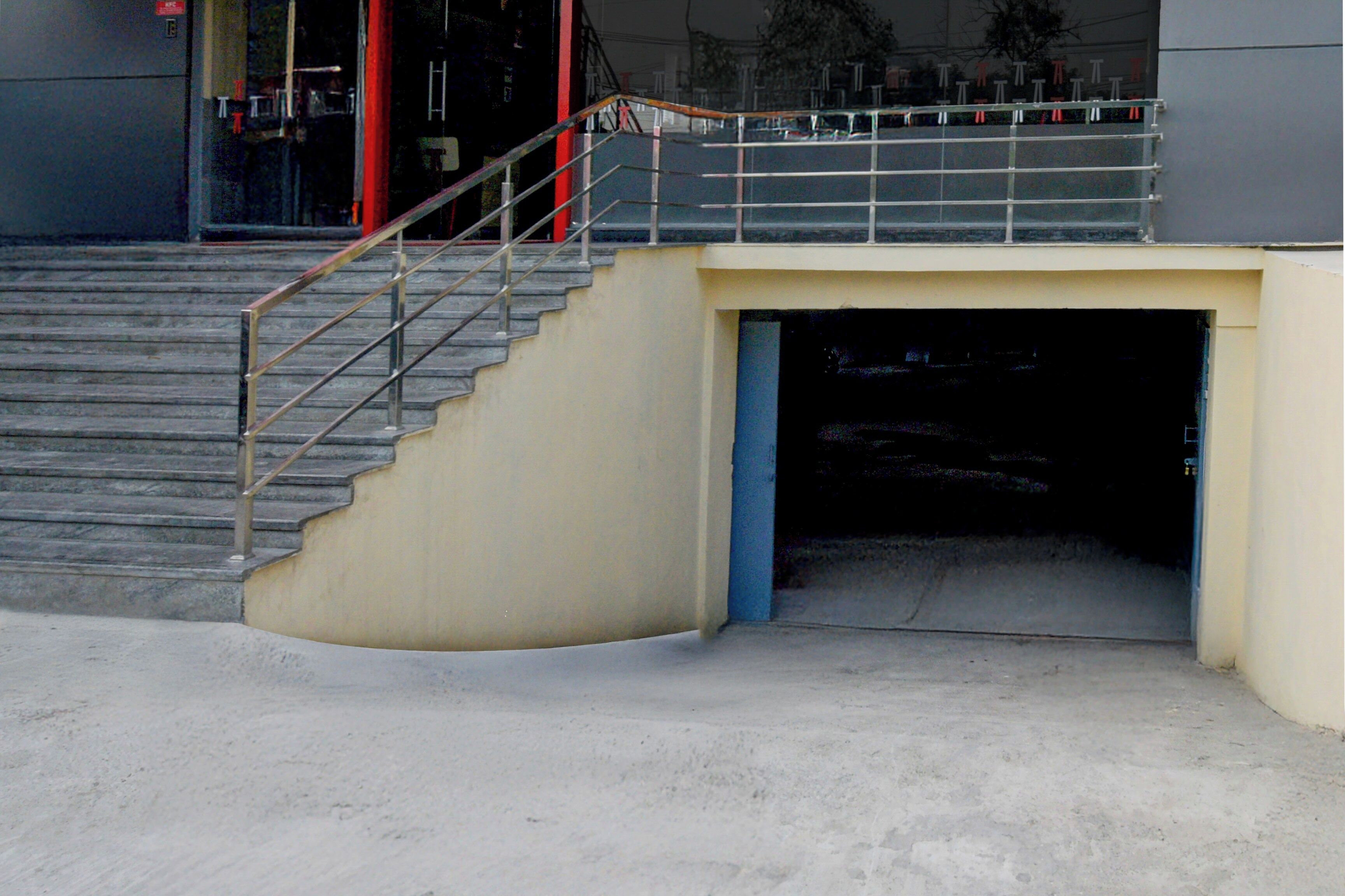 Eine Betontreppe führt zu einer Garageneinfahrt mit einem Metallgeländer und einer blauen Tür.