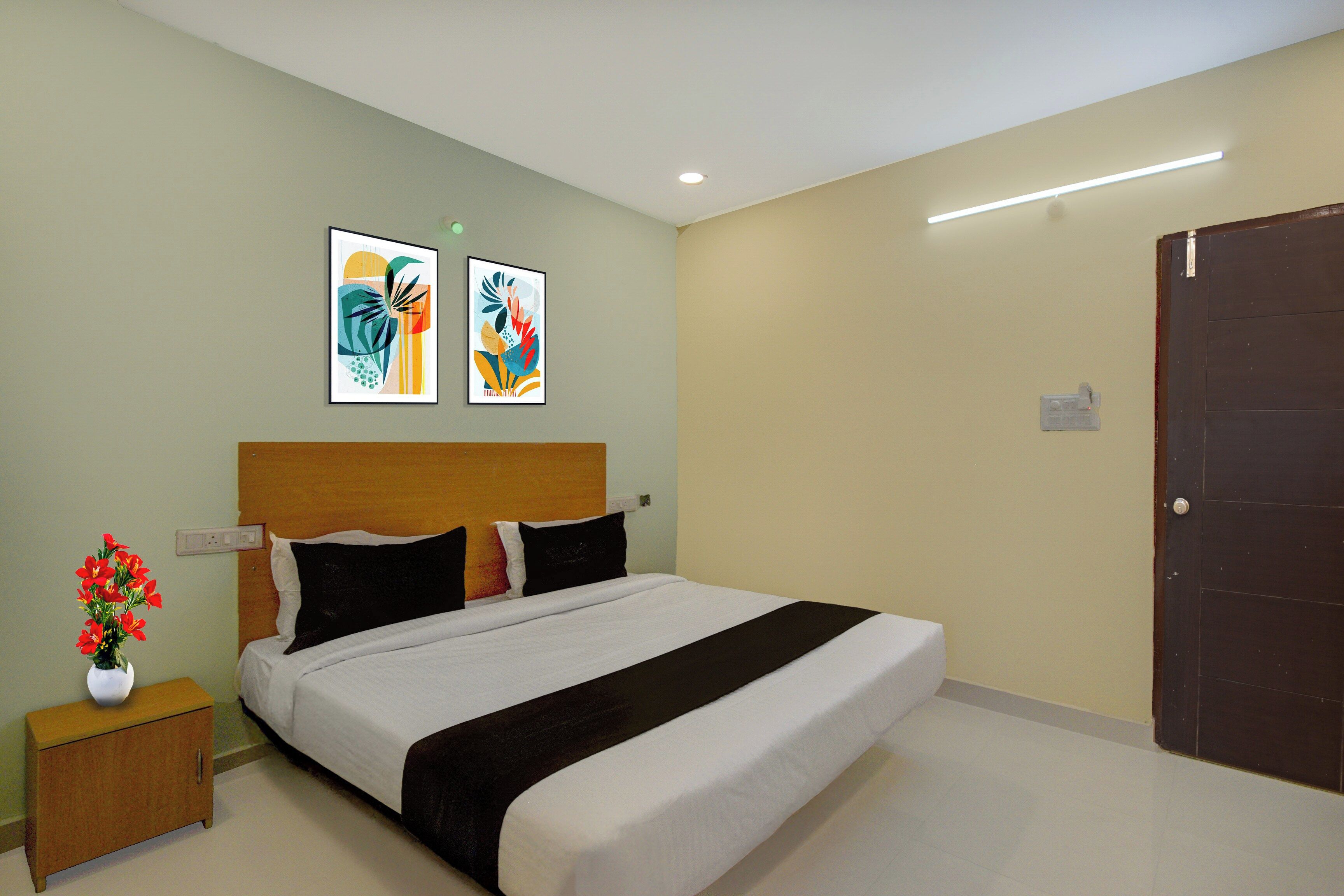 A hotel room with a bed, a nightstand, a vase of flowers, and two abstract paintings on the wall.