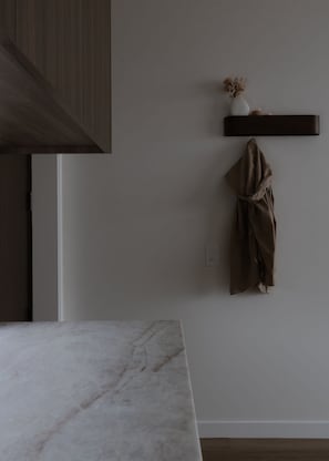Cozinha moderna com bancada de mármore, um porta-casacos pendurado e uma prateleira na parede com um vaso.