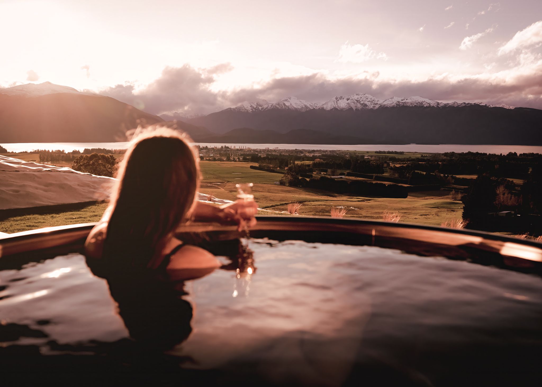 Une personne se détend dans un bain à remous, profitant d’une vue magnifique sur les montagnes et un lac.