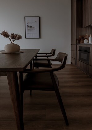 A modern dining area with a wooden table and chairs, a vase with dried flowers, and a framed picture on the wall. - Te Anau Hilltop Hideaway - Luxury retreat perched above Fiordland (Te Anau)