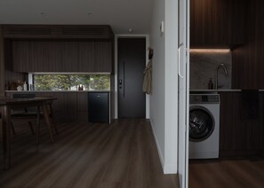 A compact kitchen with a built-in washing machine, a dining area with a view, and a dark wooden floor. - Te Anau Hilltop Hideaway - Luxury retreat perched above Fiordland (Te Anau)