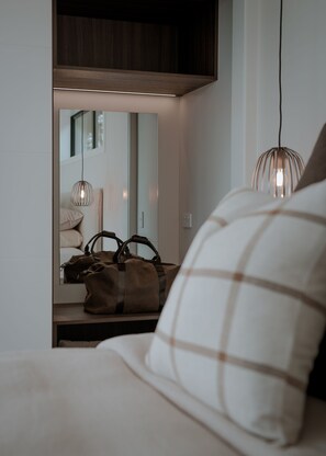 Une chambre à coucher comprenant un lit, une table de chevet, un miroir et deux lampes suspendues.