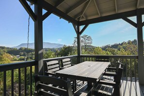 A covered outdoor area with a wooden table and benches, overlooking a mountainous landscape. - Bluff Mountain Vista • 4 Bed • 3 Bath • Stunning Views (Sevierville)