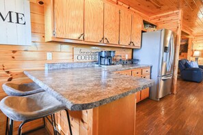 A kitchen with wooden cabinets, a granite countertop, a coffee maker, and a stainless steel refrigerator. - Bluff Mountain Vista • 4 Bed • 3 Bath • Stunning Views (Sevierville)