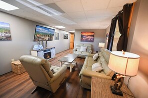 A living room with a fireplace, leather sofas, a coffee table, and a TV mounted on the wall. - Bluff Mountain Vista • 4 Bed • 3 Bath • Stunning Views (Sevierville)