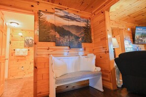 A wooden cabin interior with a bed, a television, and a painting of a mountain landscape. - Bluff Mountain Vista • 4 Bed • 3 Bath • Stunning Views (Sevierville)