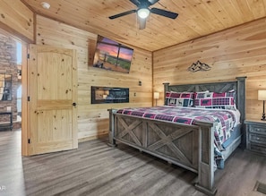 A wooden interior with a bed, a ceiling fan, a mounted TV, and a stone wall. - What a Wonderful World * 2 bed * 3 bath * sleeps 6 (Sevierville)