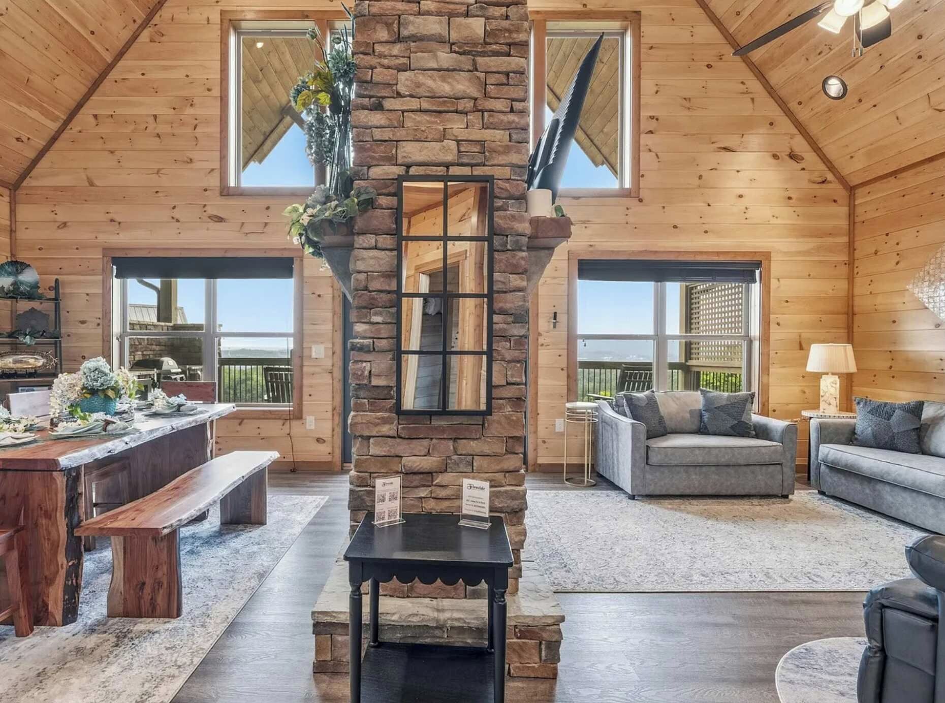 A spacious living room with wooden walls, a stone pillar, and a large window.