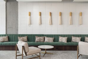 Un sofá verde con cojines estampados, una mesa redonda blanca y una pared con flecos colgantes.