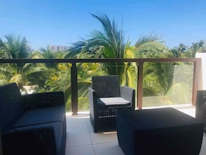 Un balcón con mobiliario de mimbre y vista a palmeras.
