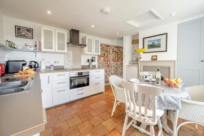 Een moderne keuken met witte kasten, een inbouwoven en een eethoek met een witte tafel en stoelen.