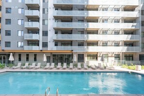 Ein modernes Gebäude mit Schwimmbad, mehreren Balkonen und Liegestühlen.