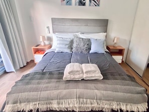A neatly made bed with a grey and white patterned bedspread, two folded white towels, and a grey headboard. - 25- Modern Space in Palermo Soho w/Pool (Buenos Aires)